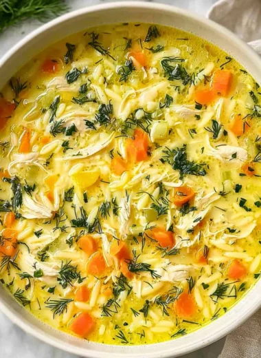 Bowl of Greek Lemon Chicken Soup garnished with fresh herbs and lemon slices.