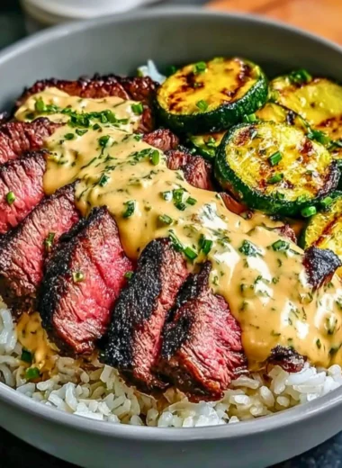Grilled steak bowl with flavorful sauce and grilled zucchini on top.