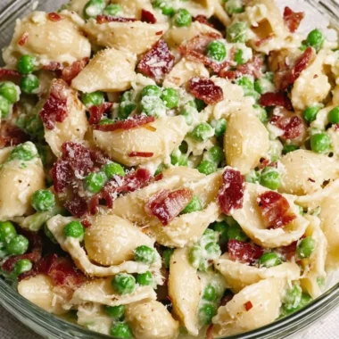 Creamy pea and bacon pasta salad served in a bowl, garnished with fresh herbs.