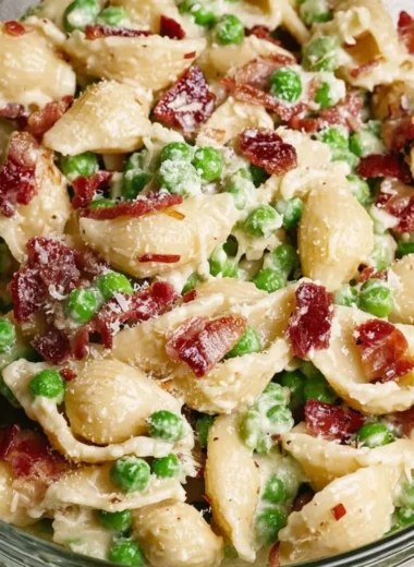Creamy pea and bacon pasta salad served in a bowl, garnished with fresh herbs.