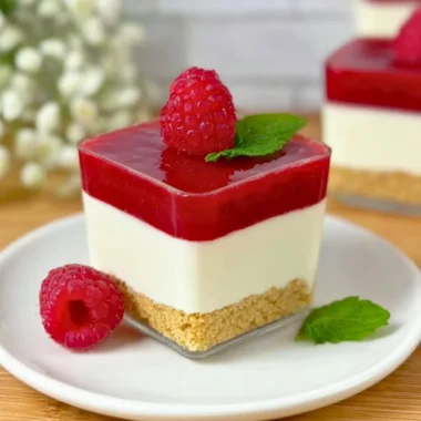 Raspberry cheesecake served in a glass with fresh raspberries and cream