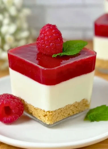 Raspberry cheesecake served in a glass with fresh raspberries and cream